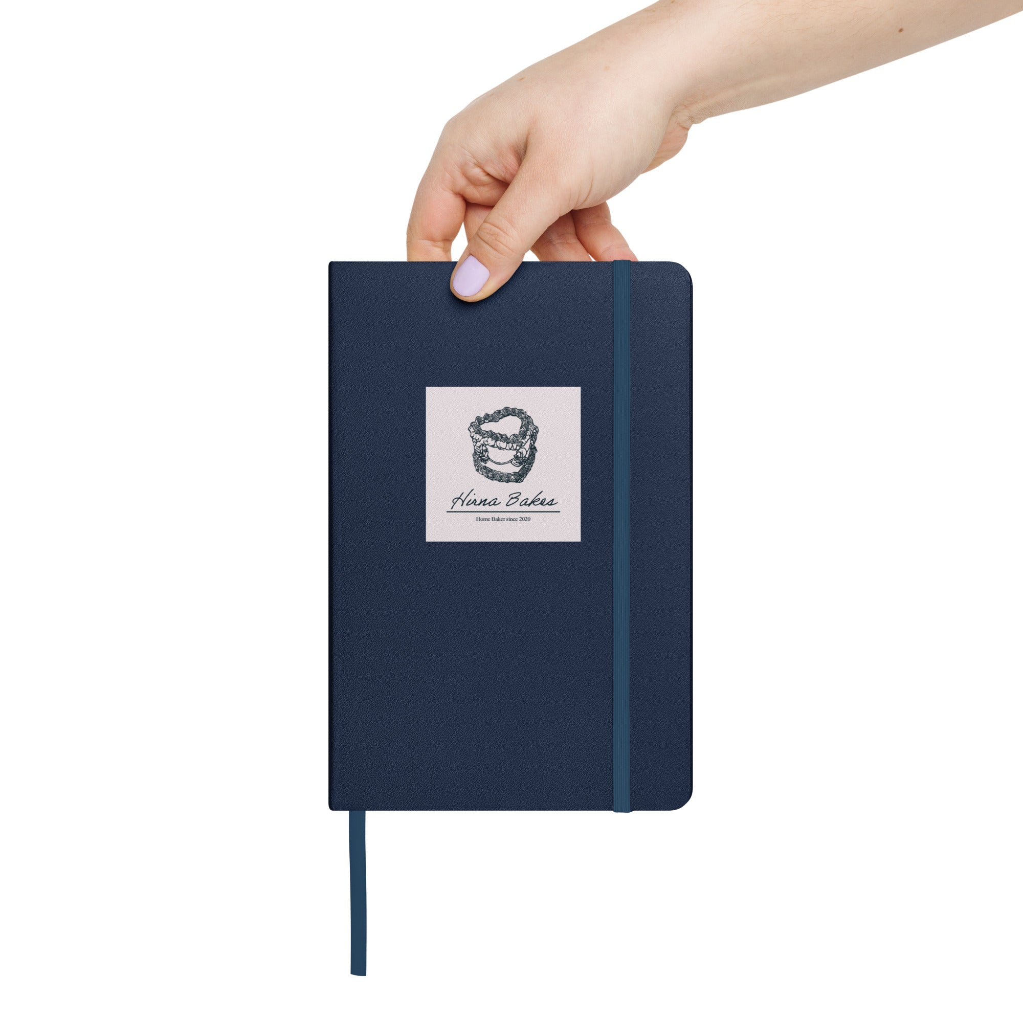 Hand holding a blue hardcover notebook with Hirna Bakes logo sticker on the front