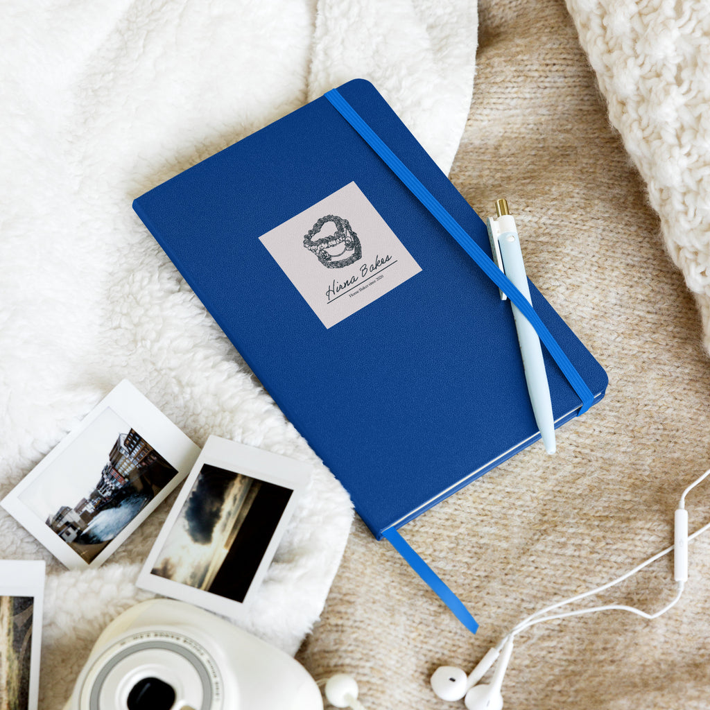 Blue hardcover notebook with Hirna Bakes logo styled with pen and instant camera photos, handmade gift from Hirna Bakes Buckinghamshire