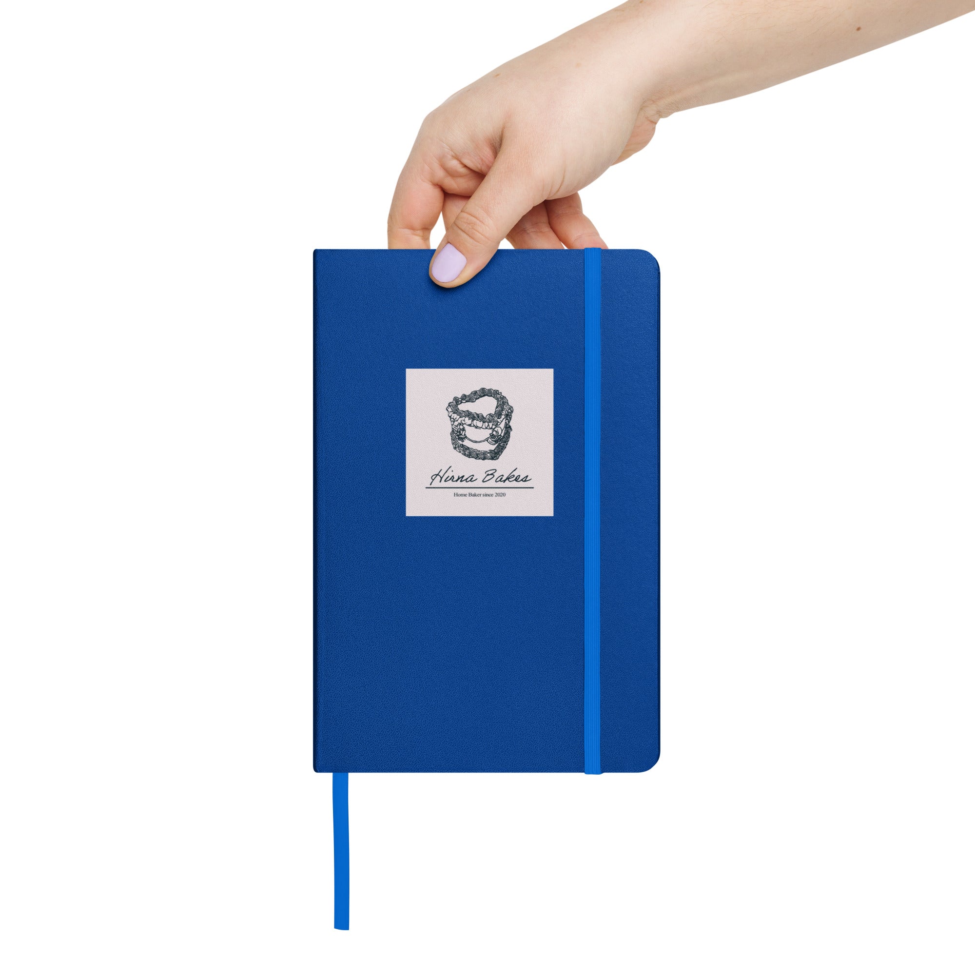 Hand holding a blue hardcover notebook with Hirna Bakes logo sticker on the front